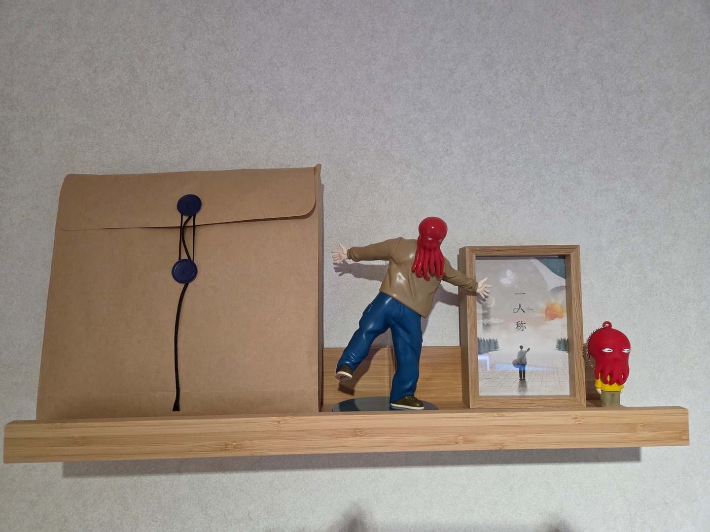 A real photo of my room's shelf, featuring a kraft paper bag, an octopus-head figure, and an "Ichininshou" framed picture
